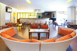 Un moderno vestíbulo de hotel con un sofá curvo, mesas de comedor y una zona de bar.