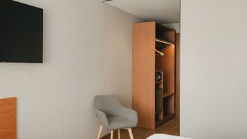Ein modernes Hotelzimmer mit einem Bett, einem grauen Sessel, einem Holzschrank und einem an der Wand befestigten Flachbildfernseher.
