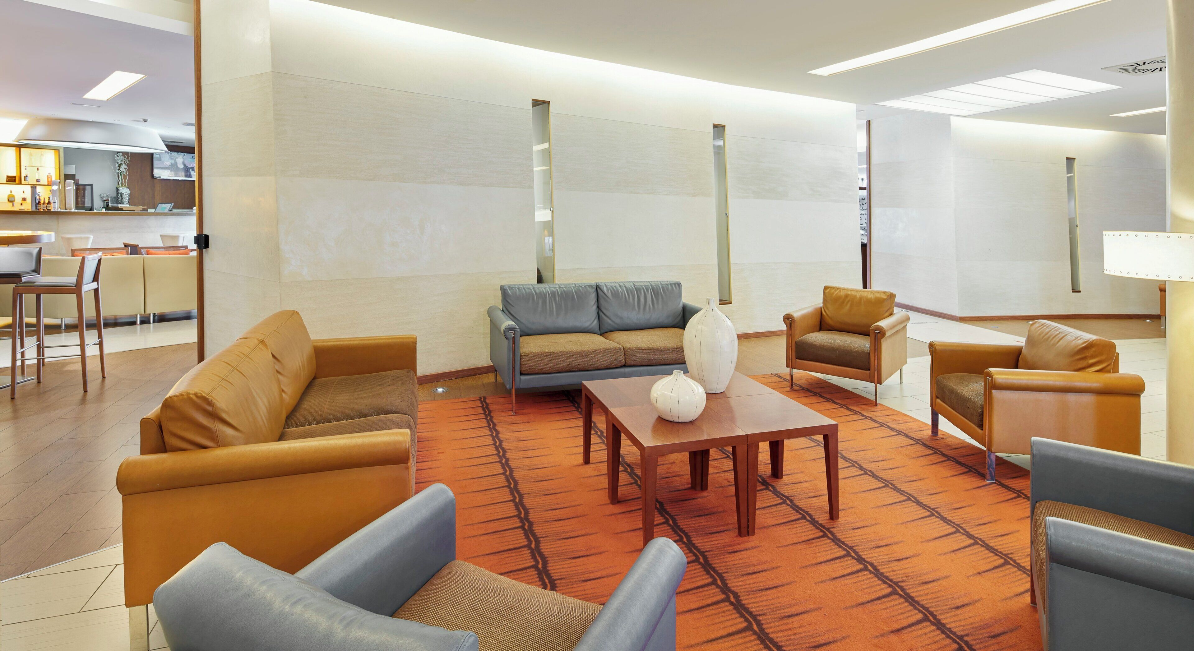 Un moderno vestíbulo de hotel con sofás de cuero, una mesa de centro de madera y una alfombra estampada.