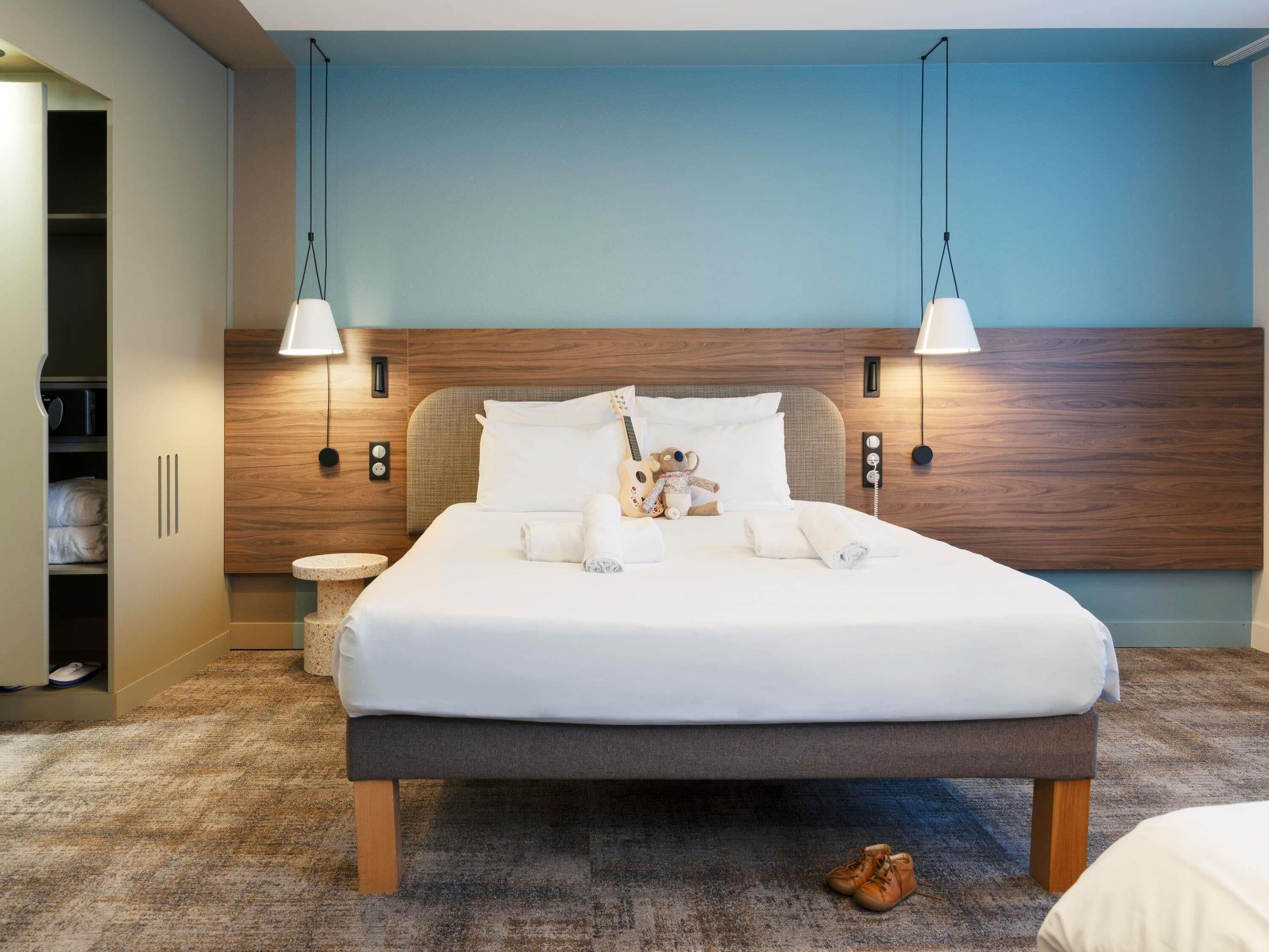 Una habitación de hotel con una cama grande, lámparas de noche, un cabecero de madera y un armario con espejo.