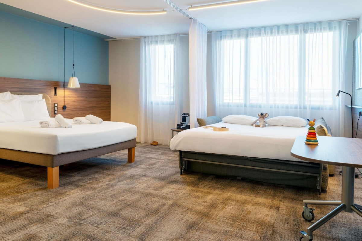 Habitación de hotel con dos camas, un escritorio y una silla con ruedas.