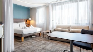 Una habitación de hotel moderna con cama, sofá, una mesita y una lámpara.
