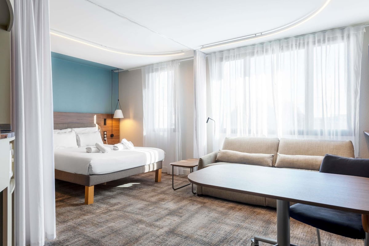 Una habitación de hotel moderna con cama, sofá, una mesita y una lámpara.