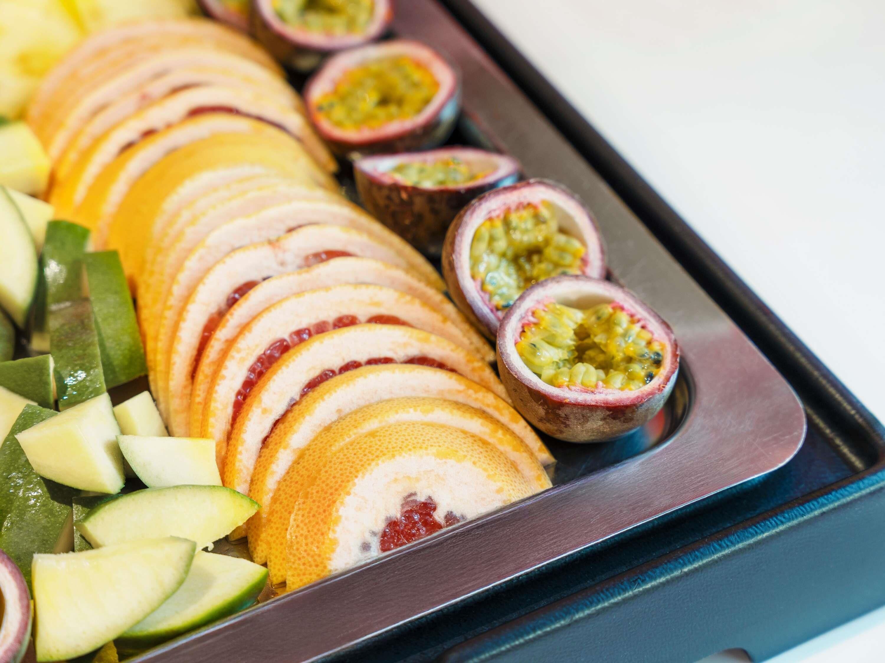 A tray of sliced fruits and passion fruit halves.