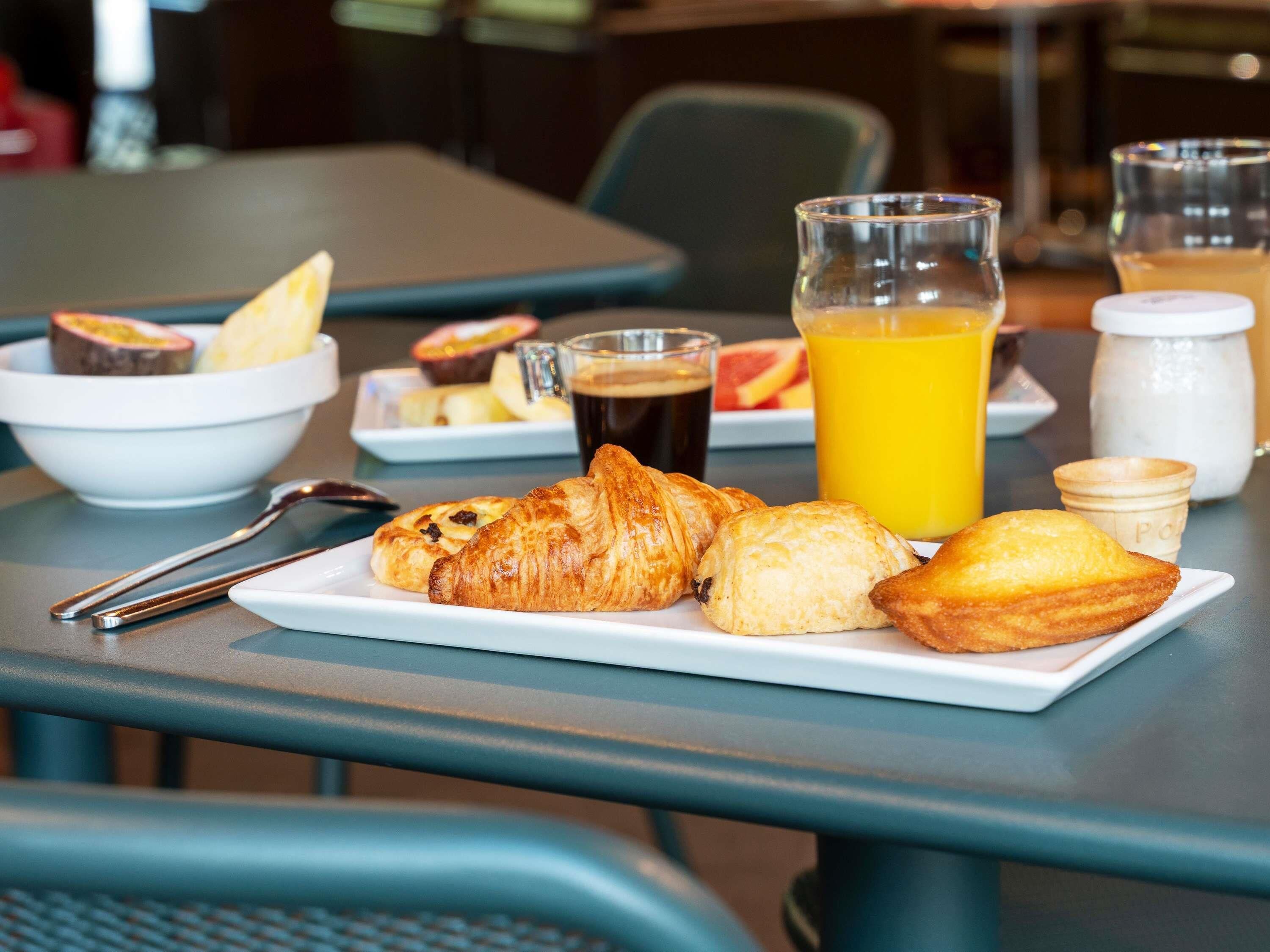 En morgenmadsopstilling med croissanter, et glas appelsinjuice og en kop kaffe på et bord.