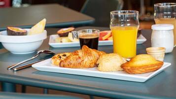 En morgenmadsopstilling med croissanter, et glas appelsinjuice og en kop kaffe på et bord.