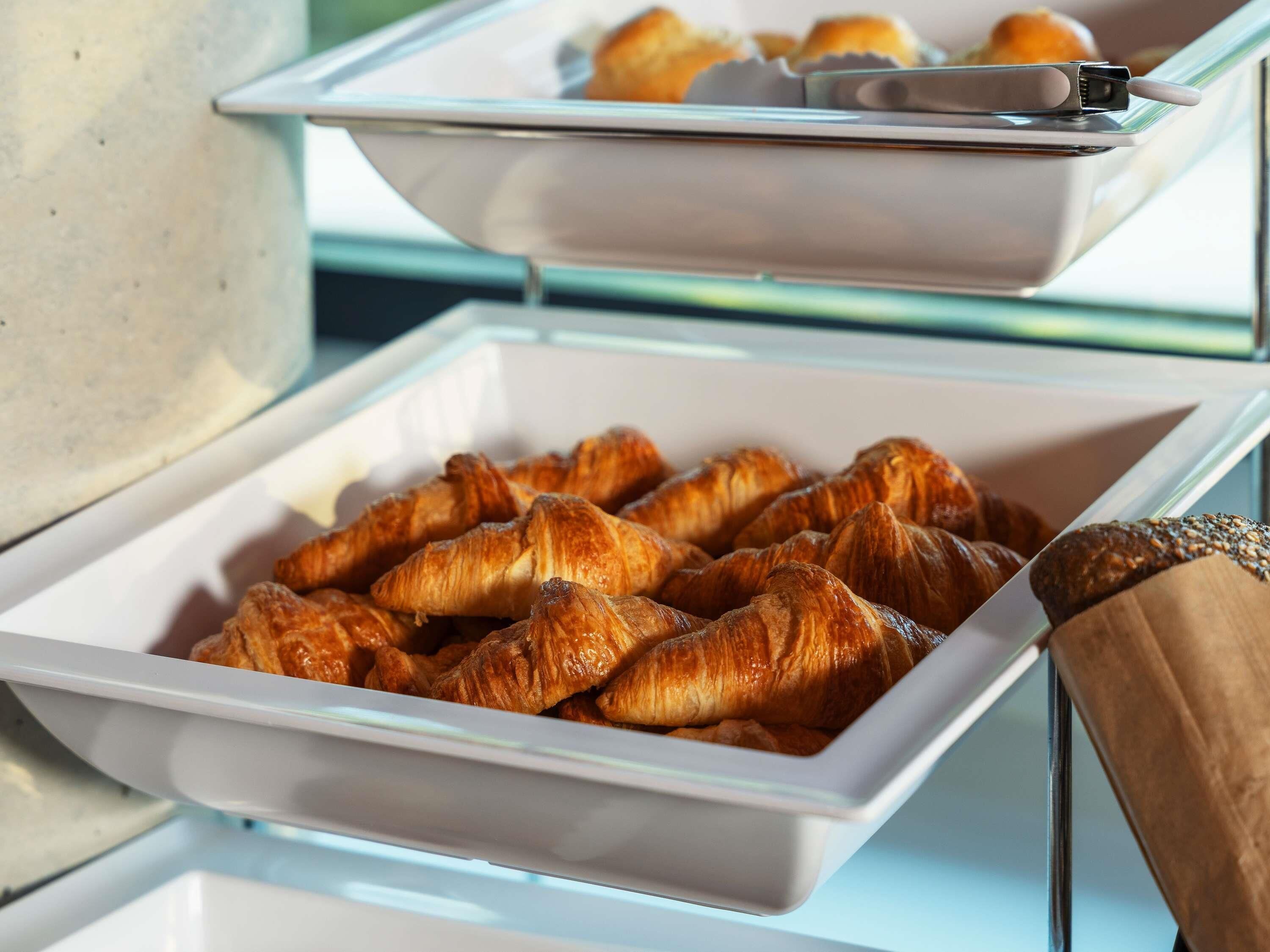 A buffet with trays of croissants and a coffee machine.