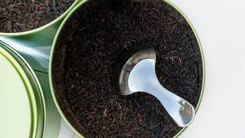 A close-up of a green tin filled with loose tea leaves and a spoon.