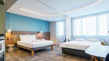 A modern hotel room with two beds, a small table, and a view of the city.