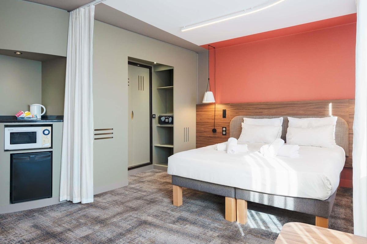 Habitación de hotel con cama, microondas, kitchenette pequeña, armario y closet.
