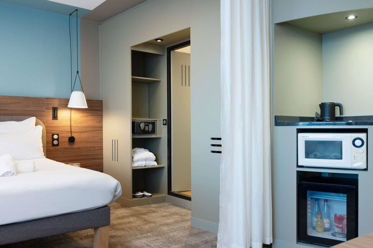 A hotel room with a bed, a wardrobe, a microwave, and a mini-fridge.
