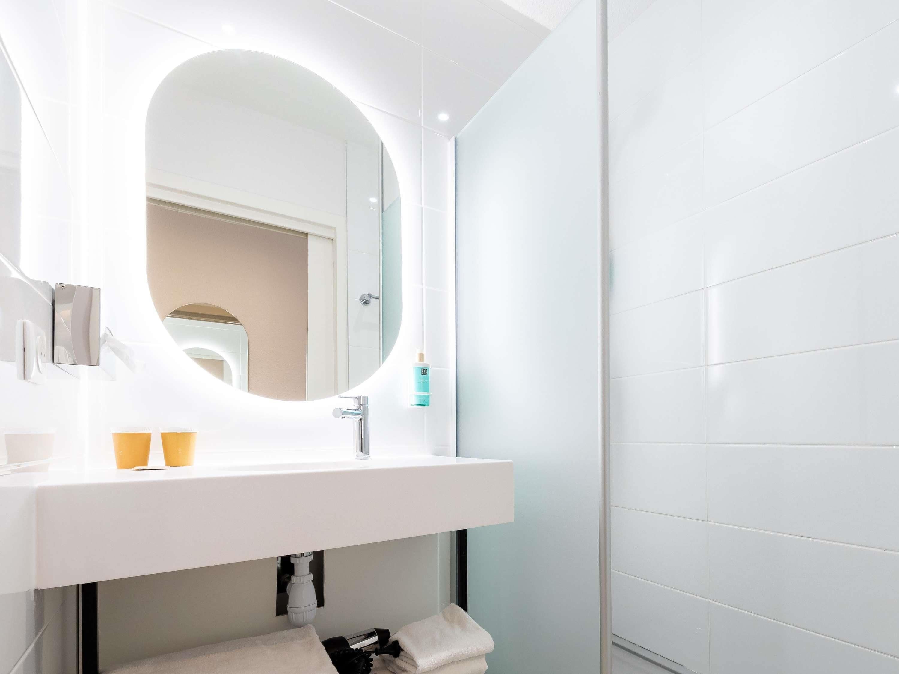 A modern bathroom with a white vanity, a round mirror, and a towel rack.