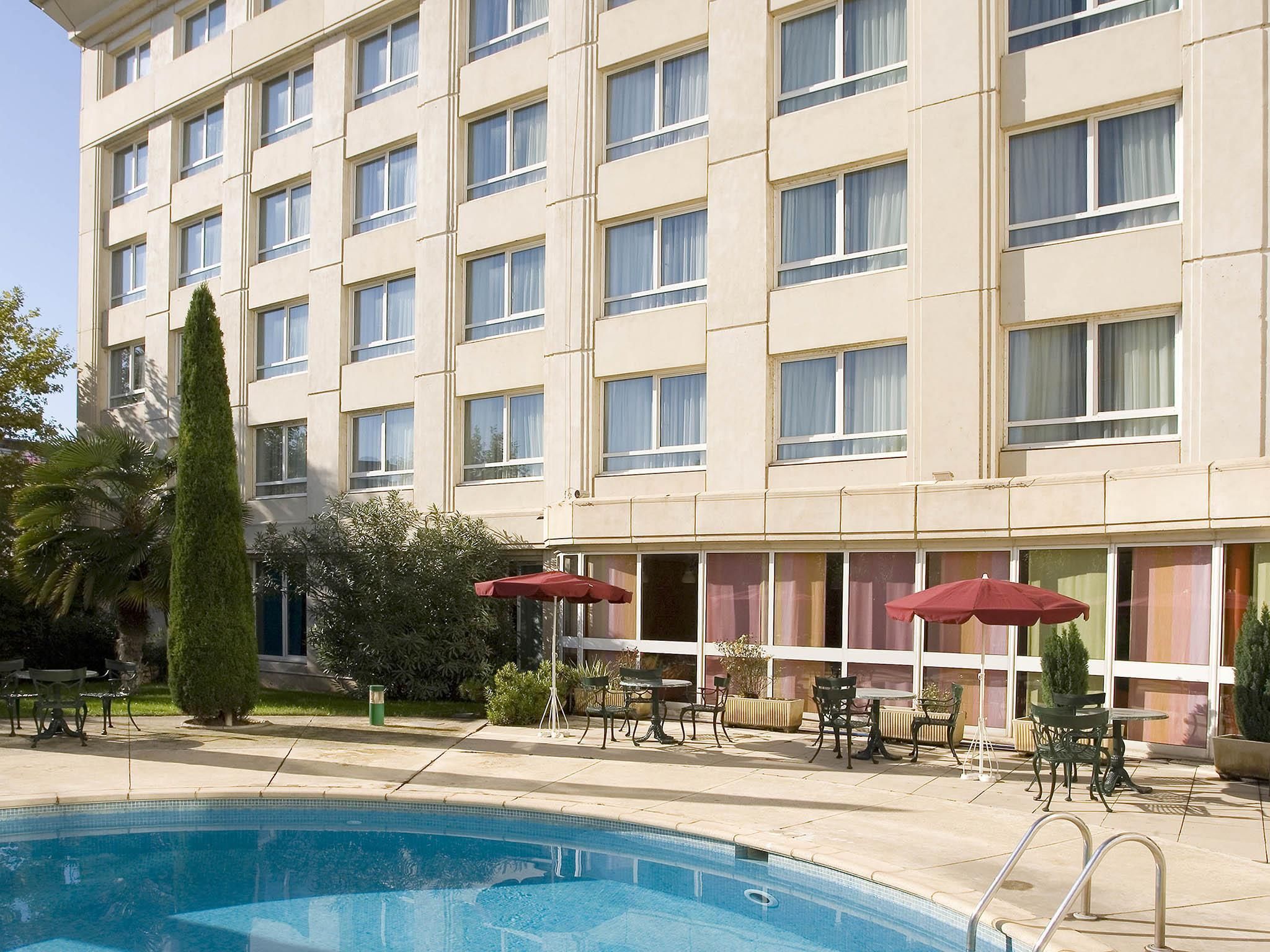 Een hotel met een zwembad, terras en een verzorgde tuin.