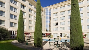 A hotel with a pool area, outdoor seating, and tall trees. - Novotel Suites Montpellier (Montpellier)