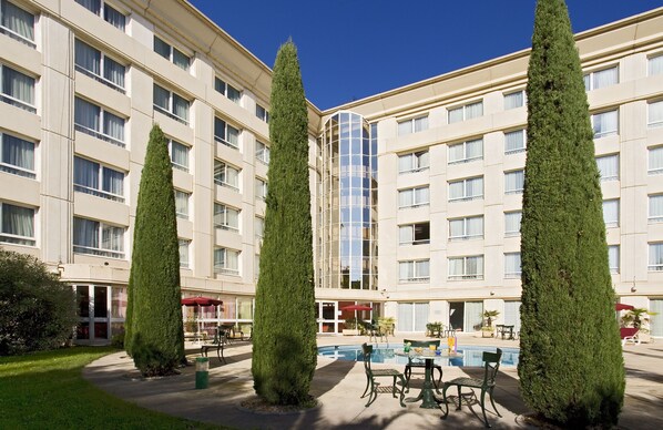 A hotel with a pool area, outdoor seating, and tall trees. - Novotel Suites Montpellier (Montpellier)