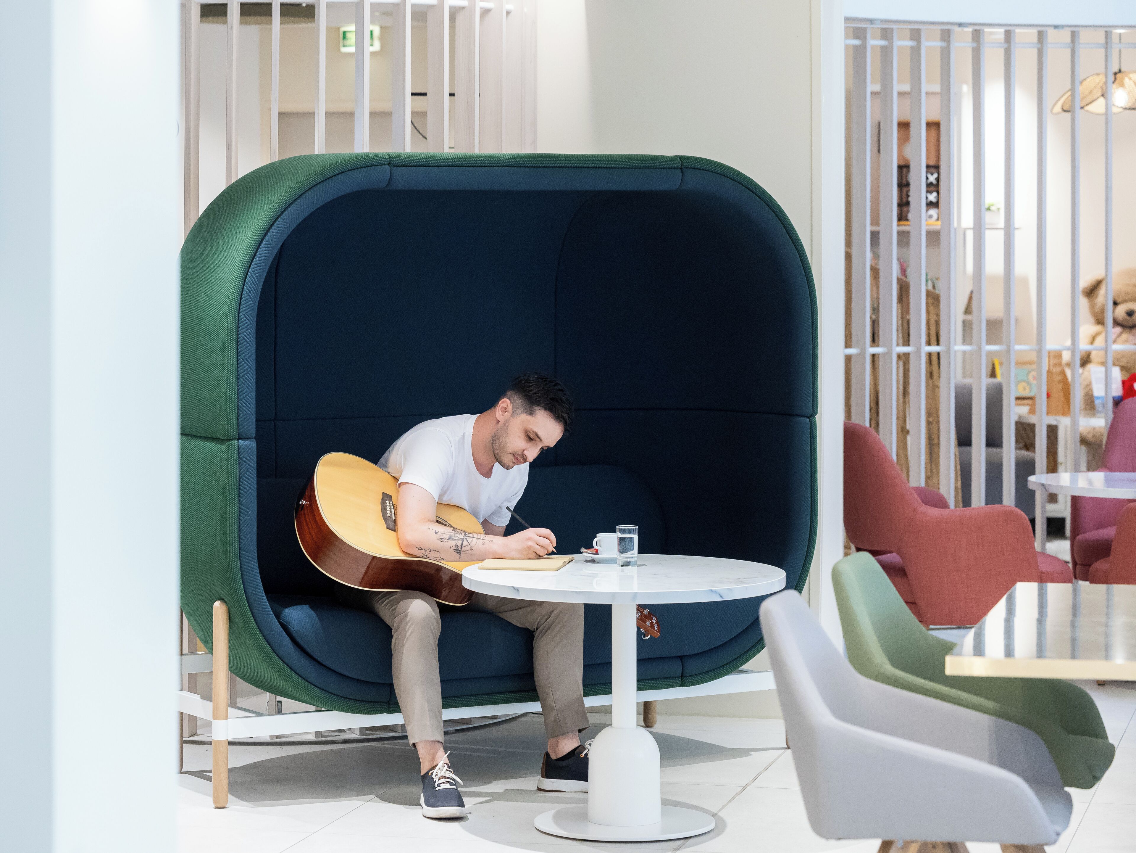 Un homme joue de la guitare dans un espace de détente accueillant et partiellement fermé, avec une table ronde et des chaises.