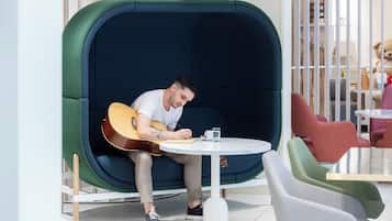 Un homme joue de la guitare dans un espace de détente accueillant et partiellement fermé, avec une table ronde et des chaises.