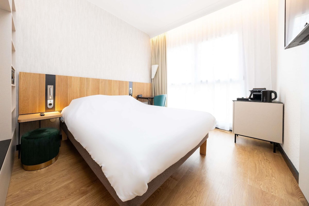 A hotel room with a bed, bedside table, lamp, and a coffee machine.