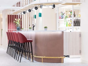 A bar area with a curved counter, red bar stools, and a metal railing. - Novotel Suites Montpellier (Montpellier)