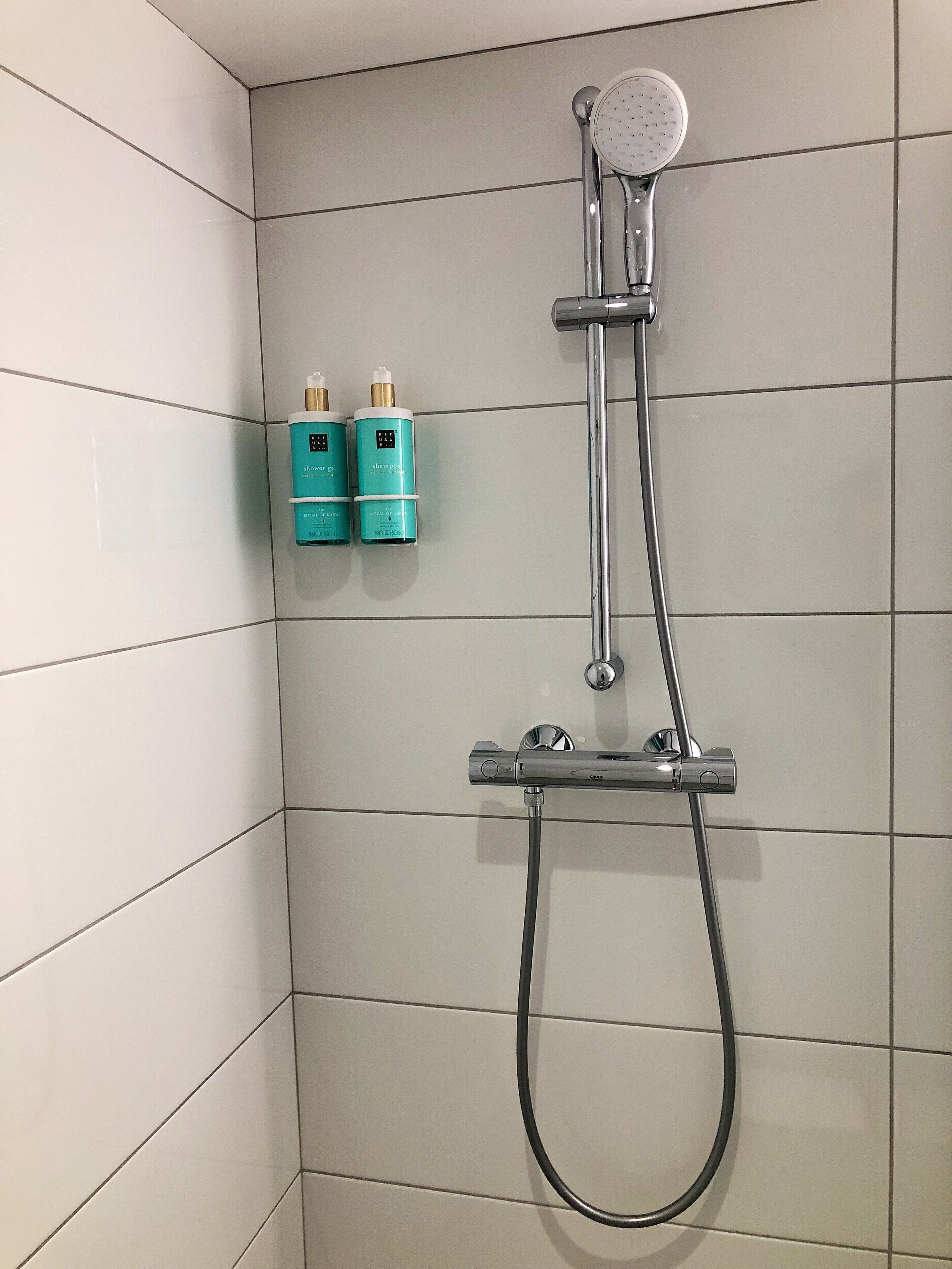 Een douche met een handdouche en een extra douchestraal, bevestigd aan een betegelde muur.