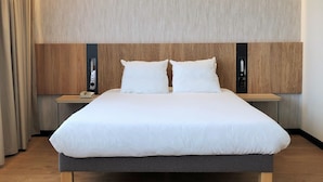 A modern hotel room with a large bed, wooden headboard, bedside tables, and a wall-mounted phone. - Novotel Suites Montpellier (Montpellier)