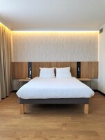 Una habitación de hotel moderna con una cama grande, cabecera de madera, mesitas de noche y un teléfono montado en la pared.