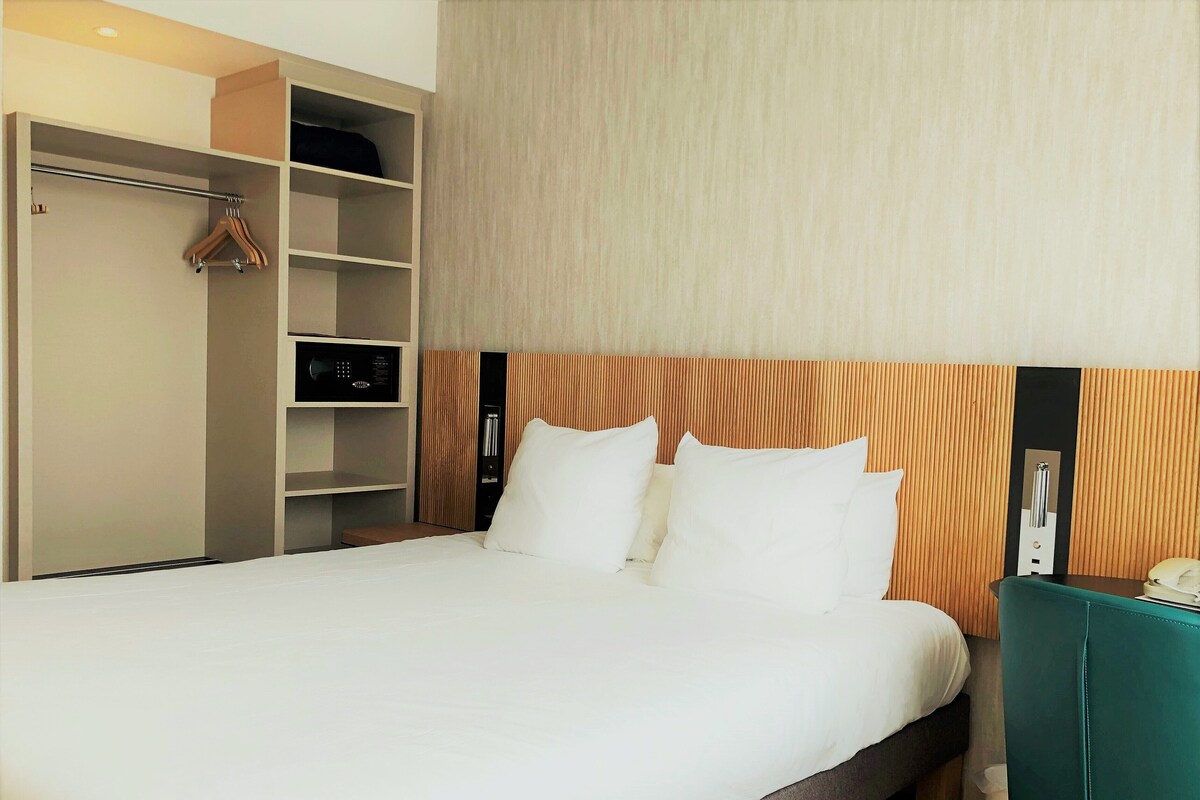 Habitación de hotel con cama, armario, mesita de noche y teléfono instalado en la pared.