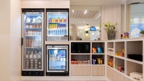 Una kitchenette con cuatro refrigeradores, un microondas y estantes llenos de bocadillos y condimentos.