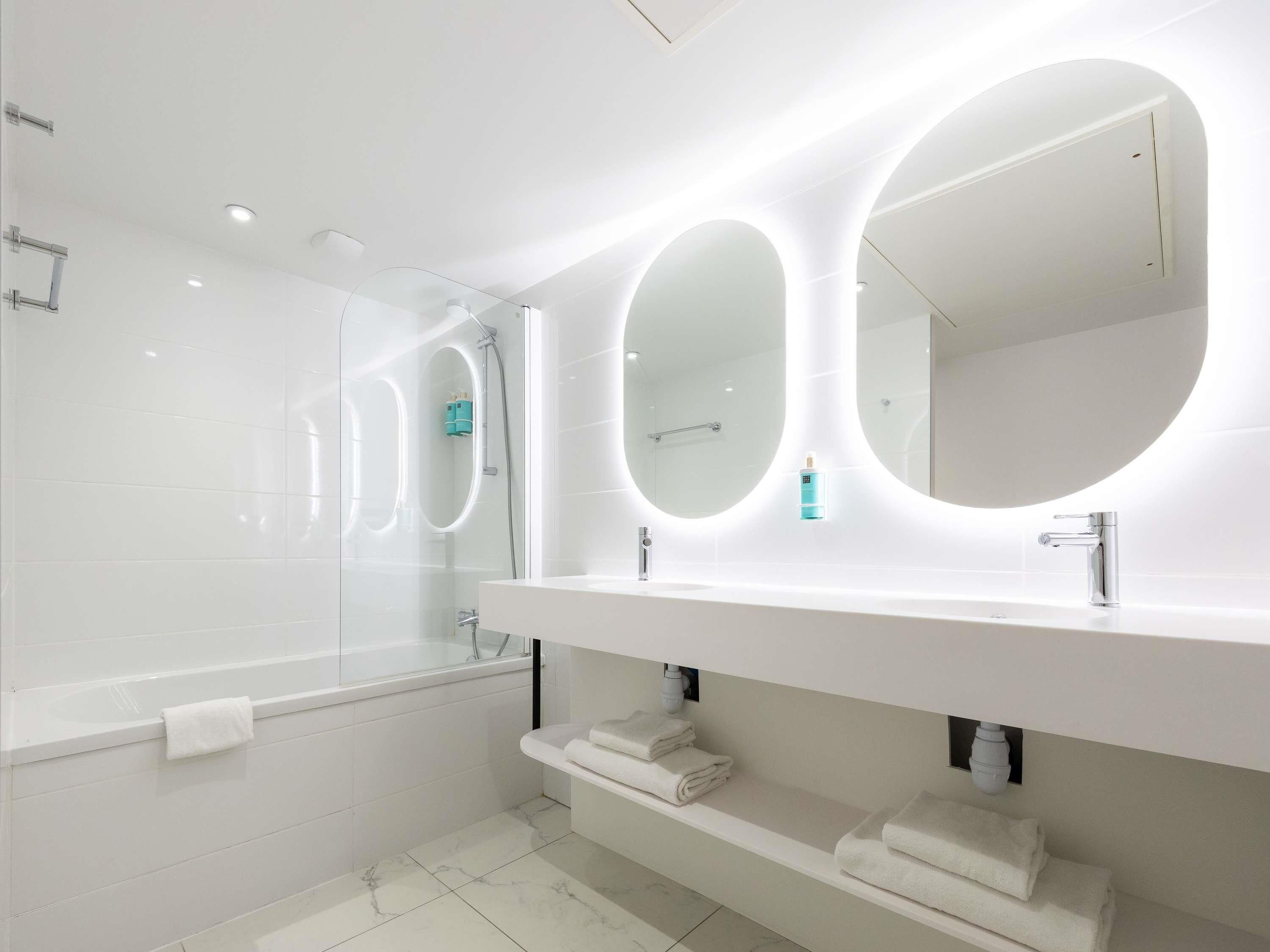 A modern bathroom with a large mirror, a bathtub, and a vanity with a towel rack.