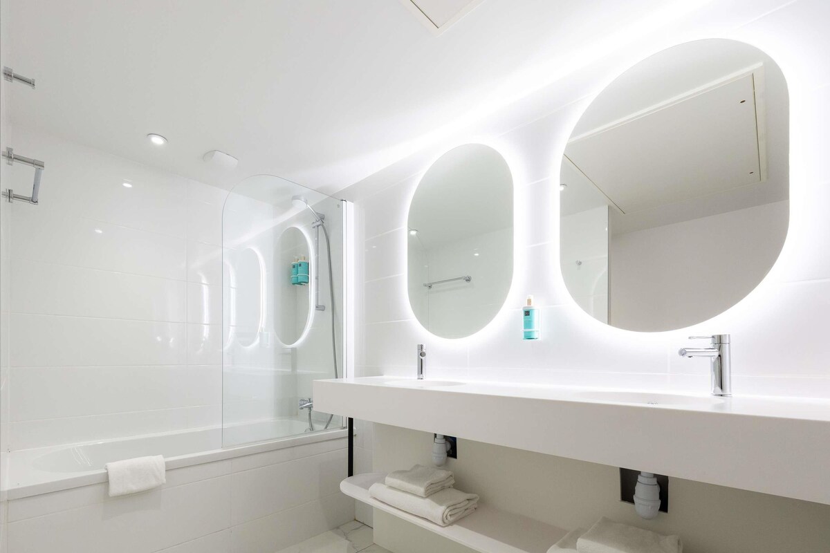 A modern bathroom with a large mirror, a bathtub, and a vanity with a towel rack.