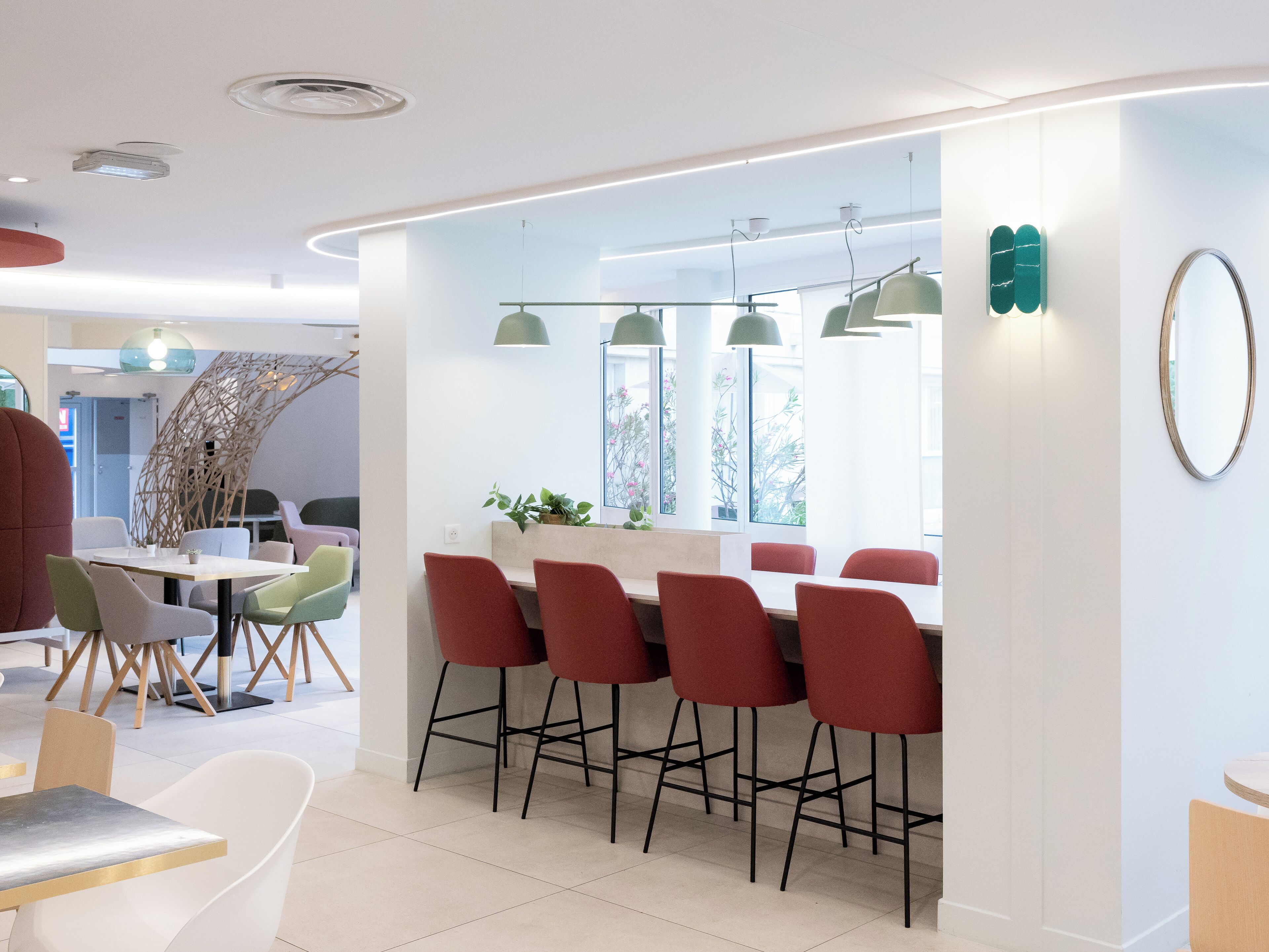 A modern dining area with a bar, red bar stools, and a mix of white and green chairs.