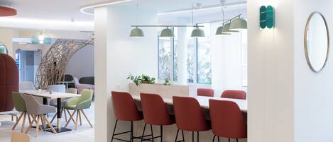 A modern dining area with a bar, red bar stools, and a mix of white and green chairs.