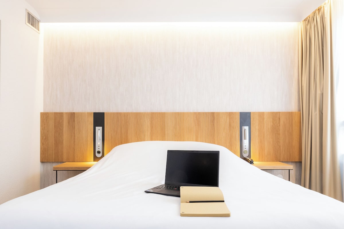 Una habitación de hotel con una cama, una laptop y un cuaderno sobre la cama.