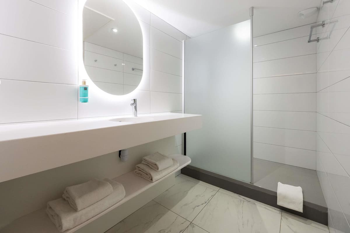 A modern bathroom with a white vanity, a round mirror, a glass shower enclosure, and neatly folded towels.