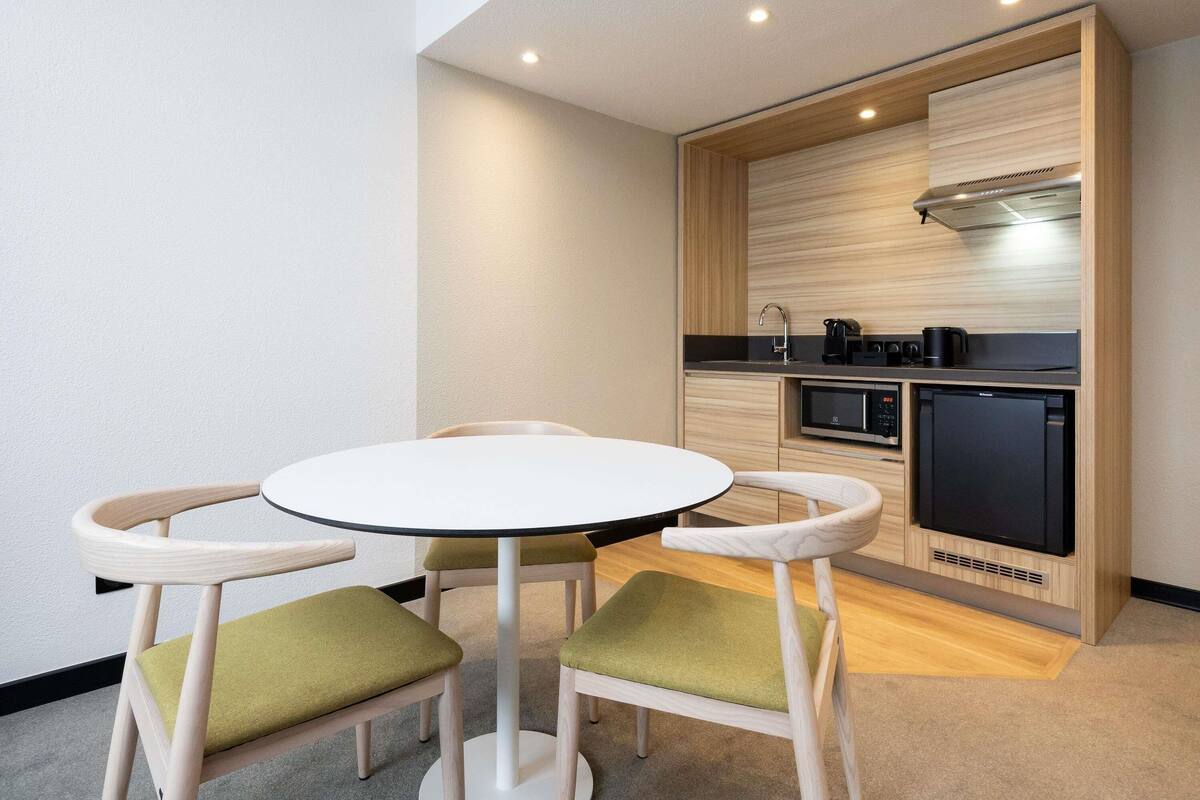 A modern kitchen with a built-in oven, microwave, and coffee maker. There is a round table with four chairs, each with a green cushion.