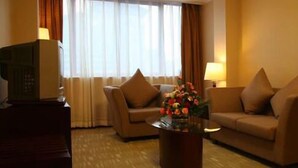 Een hotelkamer met twee banken, een bijzettafeltje met bloemen, een televisie op een standaard, en een raam met gordijnen.