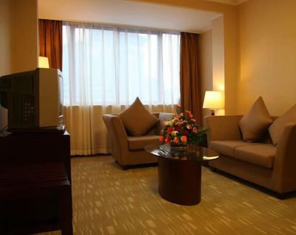 Een hotelkamer met twee banken, een bijzettafeltje met bloemen, een televisie op een standaard, en een raam met gordijnen.
