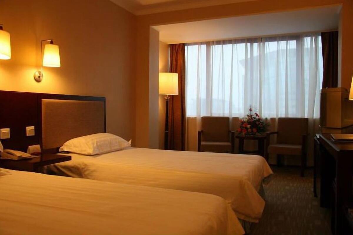 Une chambre d’hôtel avec deux lits, un bureau, une chaise et une petite table avec une lampe.