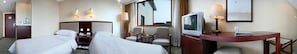 A hotel room with two beds, a TV, a desk with a lamp, and a window with a view of a building.