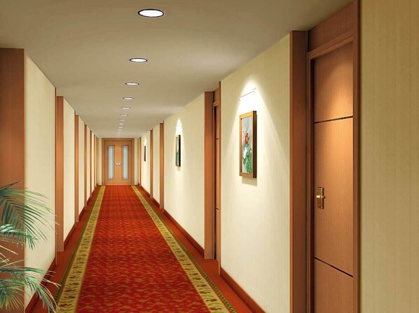 Een hotelgang met een rode loper, houten deuren en inbouwverlichting.