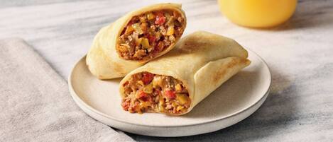 A plate with two burritos and a glass of orange juice on a table.