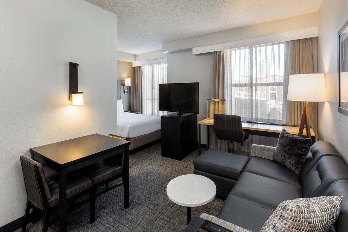 A hotel room with a bed, a TV, a desk, a sofa, and a small table.