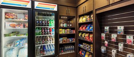 Una tienda de comestibles con congeladores refrigerados, estantes llenos de bebidas, snacks y artículos para el hogar.