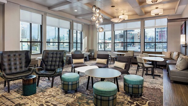 A spacious lobby with leather sofas, round tables, and ottomans, featuring large windows and modern lighting fixtures.