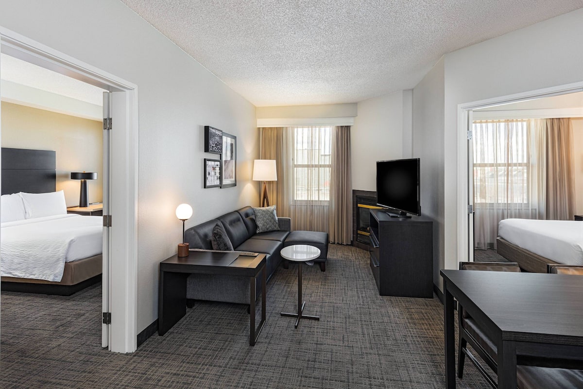 A hotel room with a bed, a sofa, a desk, a TV, and a window with curtains.