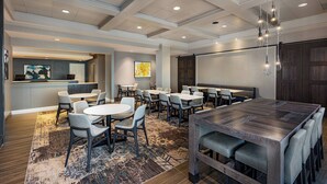 A conference room with a large table, multiple chairs, a projector screen, and a small bar area.