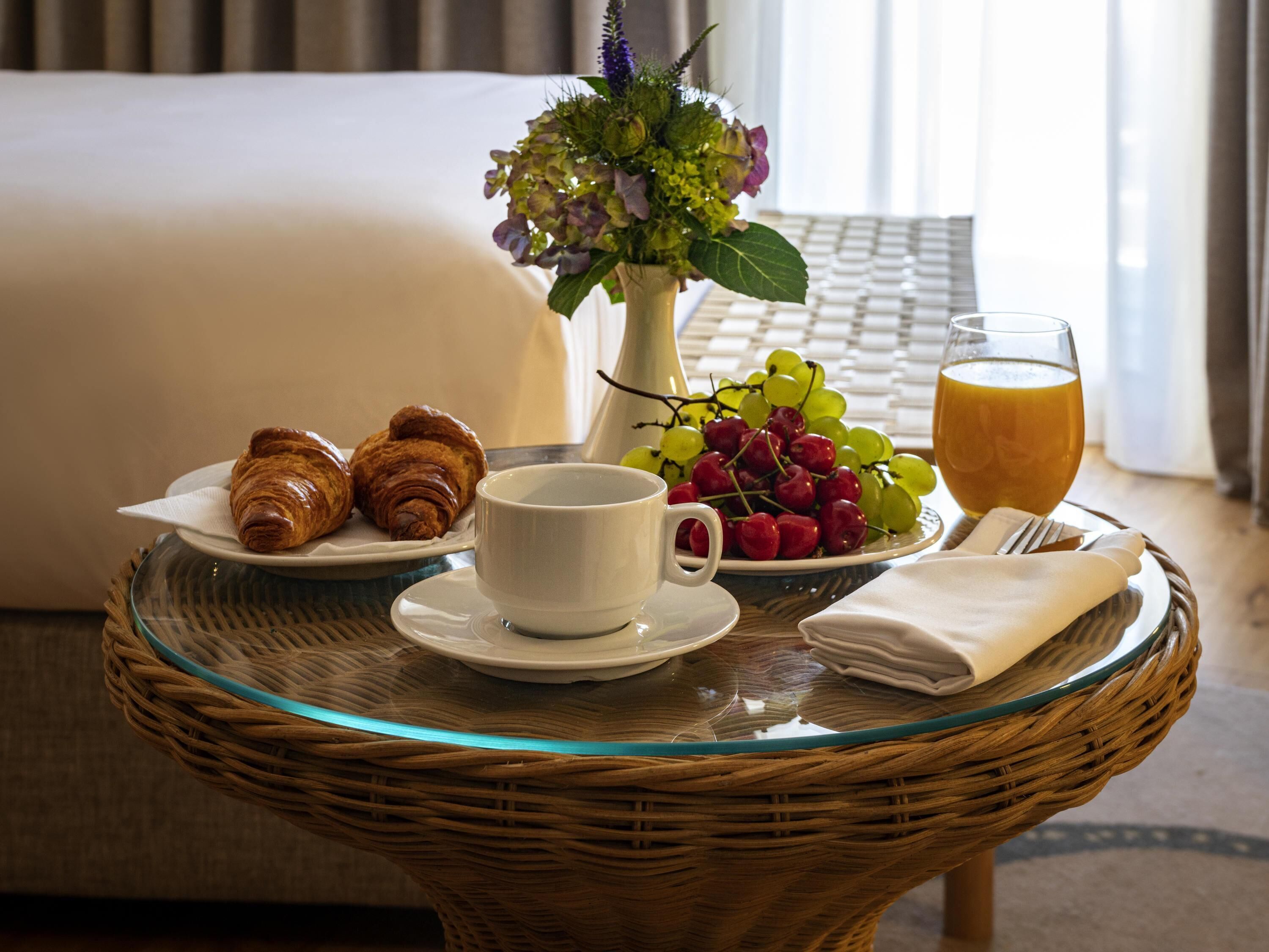 A breakfast setting with croissants, a cup of coffee, a bowl of fruit, and a glass of orange juice on a glass table.