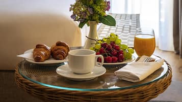 A breakfast setting with croissants, a cup of coffee, a bowl of fruit, and a glass of orange juice on a glass table.