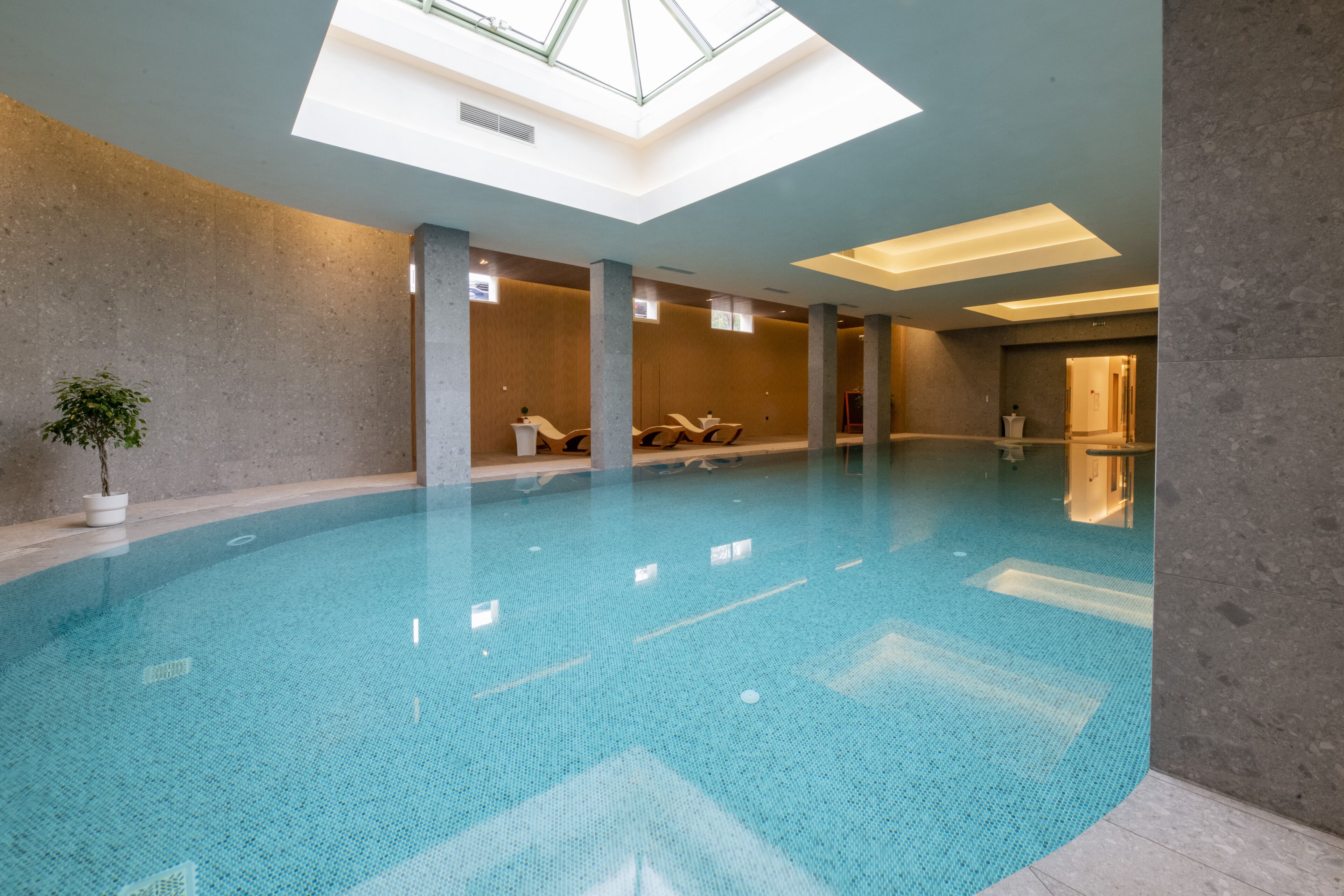 Una piscina interior con tragaluces, paredes de piedra y sillas de descanso.