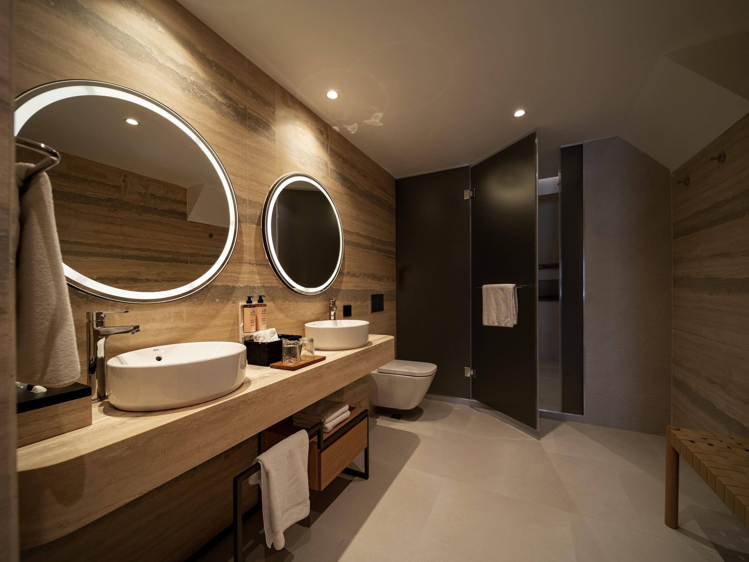 Ein modernes Badezimmer mit zwei Waschbecken, einem großen Spiegel und einer begehbaren Dusche.
